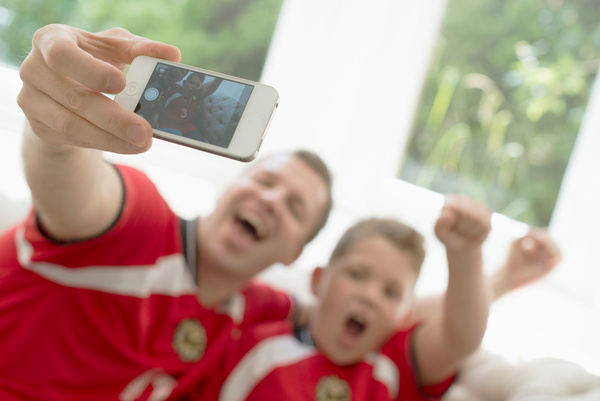 Father and son (10-12 years) watching sports event, making selfie